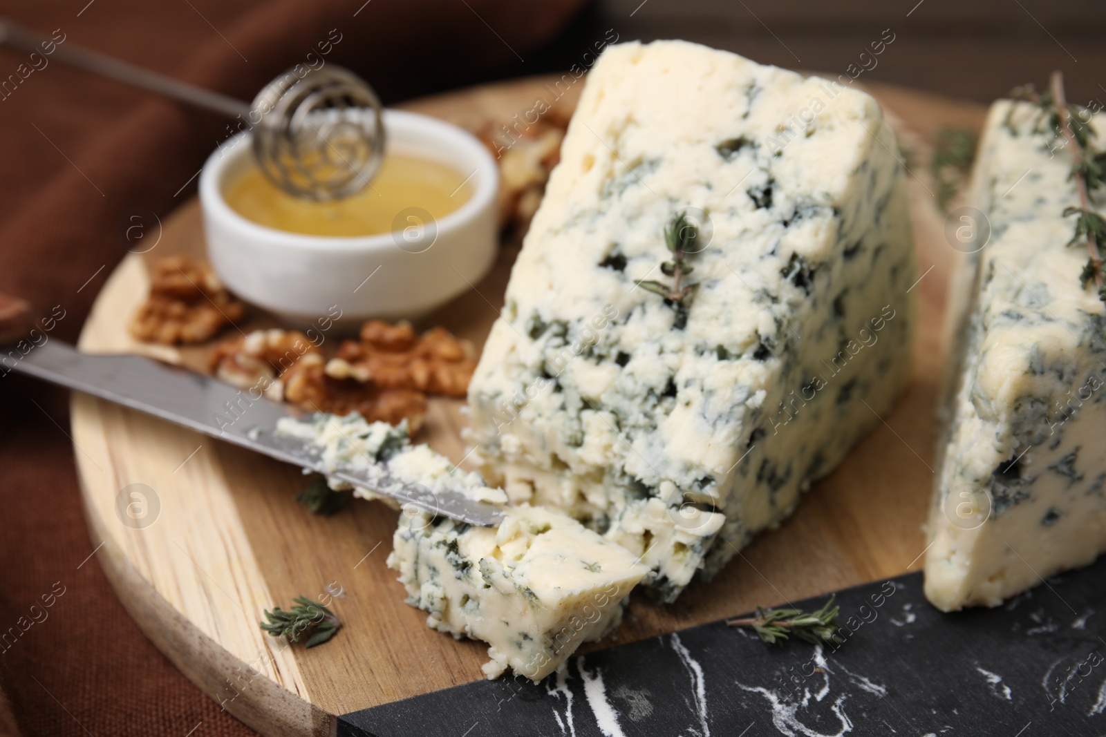 Photo of Tasty blue cheese with thyme, honey and walnuts on wooden board, closeup