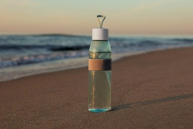Photo of Glass bottle with water on wet sand near sea at sunset