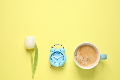 Photo of White tulip, alarm clock and coffee on yellow background, flat lay with space for text. Good morning