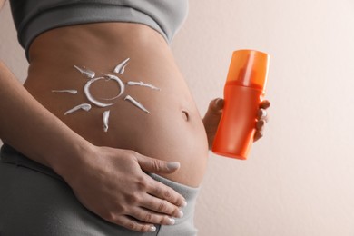 Pregnant woman with sun protection cream on beige background, closeup