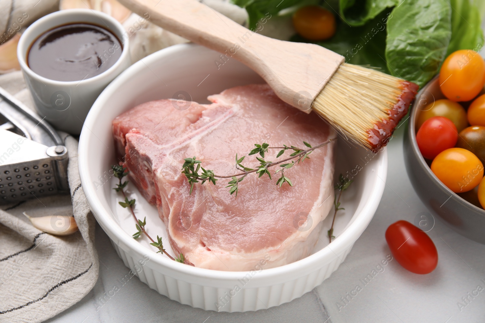 Photo of Raw meat, thyme, brush with marinade and products on light table, closeup