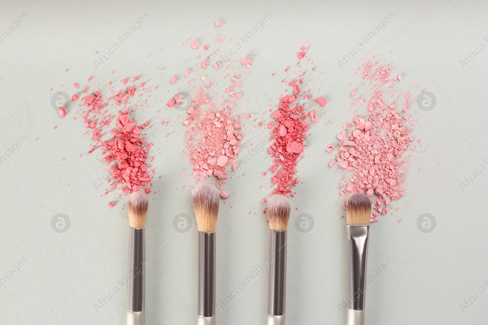 Photo of Makeup brushes and scattered eye shadows on light grey background, flat lay