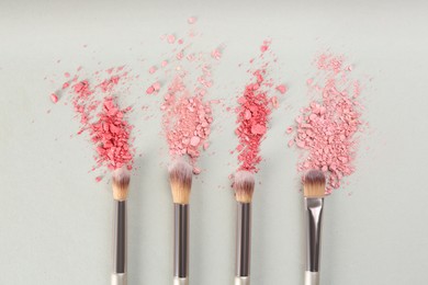 Photo of Makeup brushes and scattered eye shadows on light grey background, flat lay