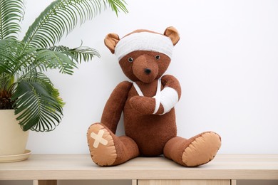 Toy bear with bandages sitting on wooden shelving unit near white wall