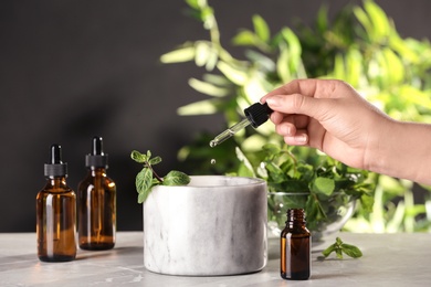Photo of Woman dripping essential oil into mortar with mint on table, closeup