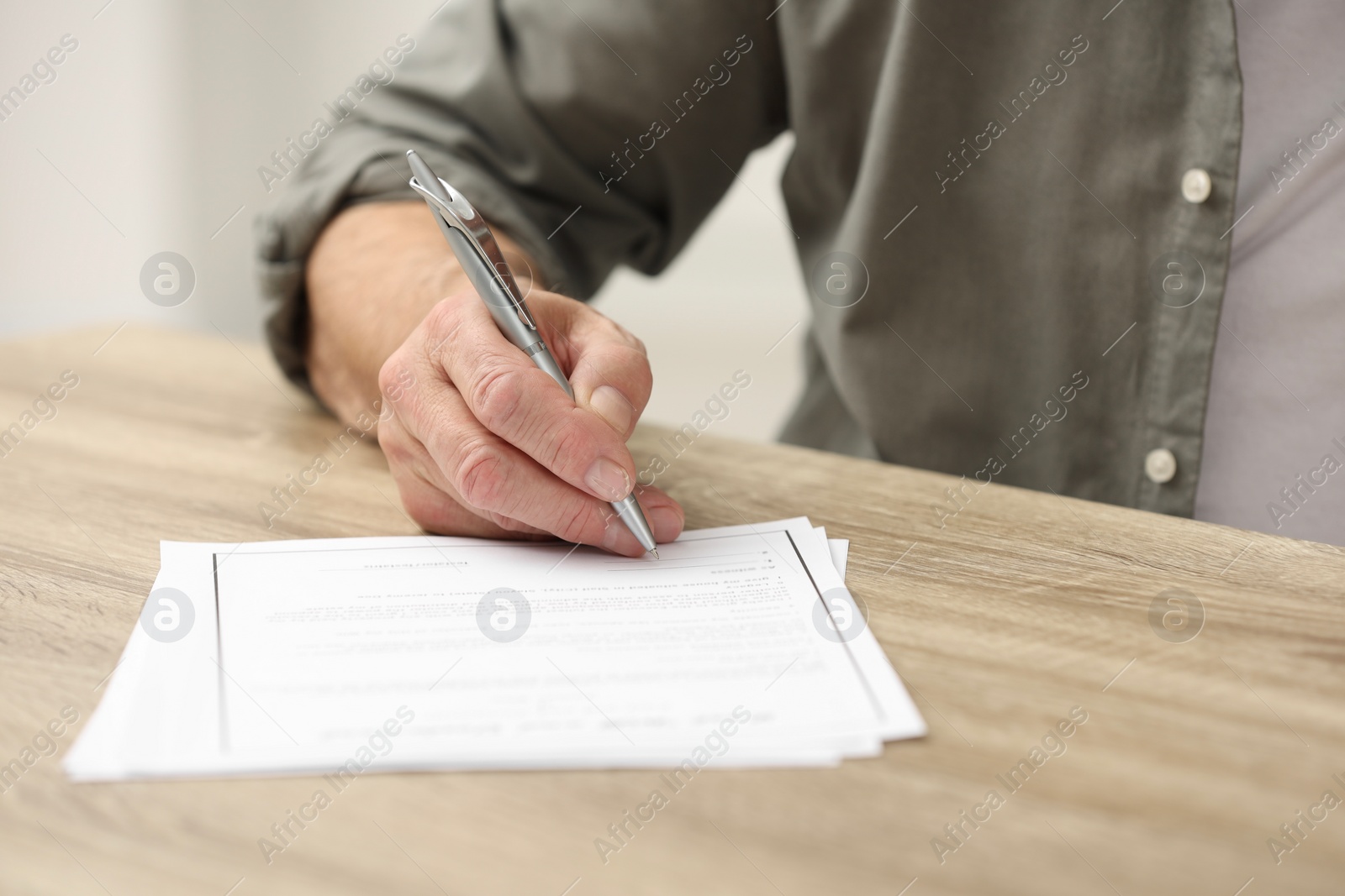 Photo of Senior man signing Last Will and Testament at wooden table indoors, closeup