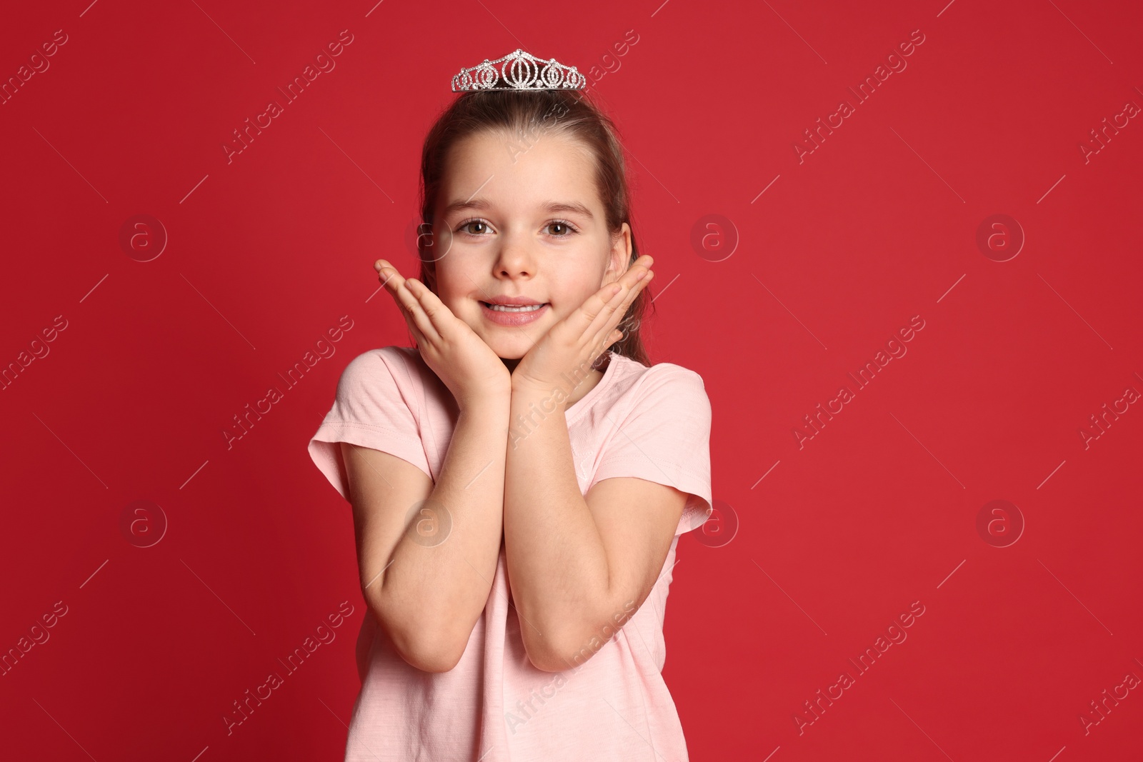 Photo of Cute girl in diadem on red background. Little princess