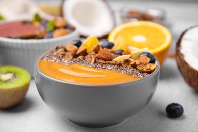 Bowl of delicious fruit smoothie with fresh orange slices, blueberries and granola on white table, closeup