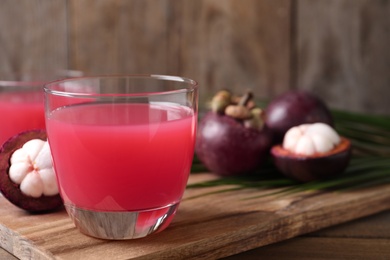 Delicious fresh mangosteen juice in glass on wooden table, space for text