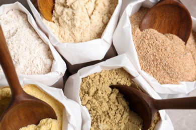 Paper bags with different types of flour and wooden spoons, closeup