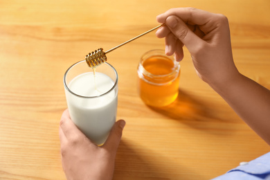 Photo of Woman adding honey to milk at table, closeup