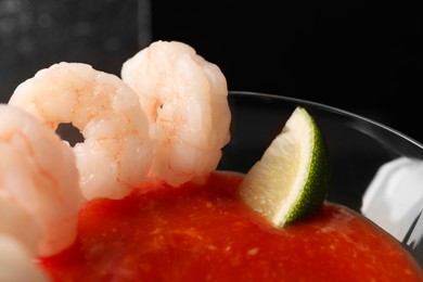 Photo of Tasty shrimp cocktail with sauce and lime in glass on dark background, closeup
