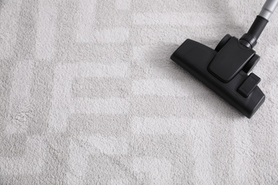 Photo of Modern vacuum cleaner on carpet indoors. Space for text