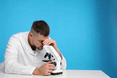 Scientist using modern microscope at table against blue background, space for text. Medical research