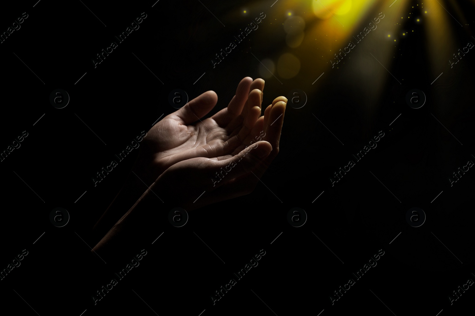 Image of Christian woman stretching hands towards holy light in darkness, closeup. Prayer and belief