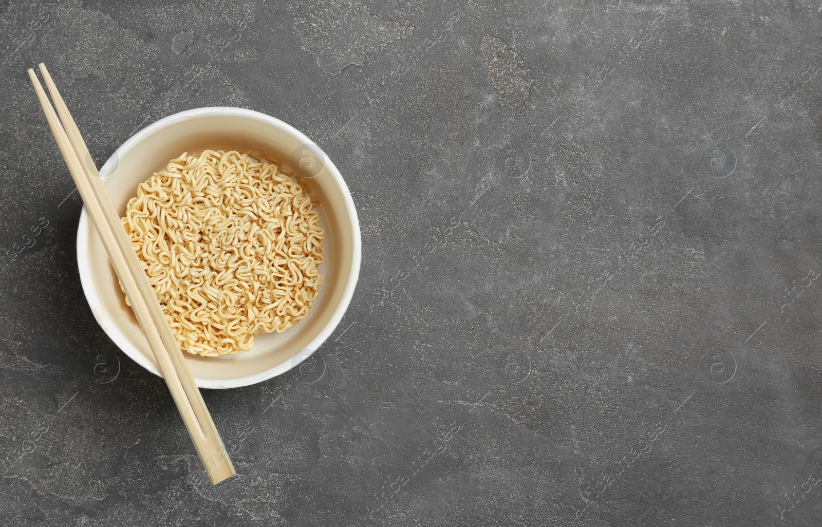 Photo of Cup of instant noodles with chopsticks on grey background, top view. Space for text