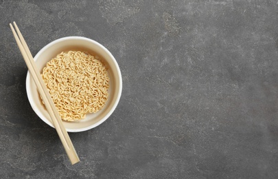 Cup of instant noodles with chopsticks on grey background, top view. Space for text