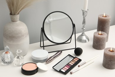 Photo of Dressing table with mirror, cosmetic products and burning candles in makeup room
