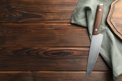 Photo of Knife, board and towel on wooden table, flat lay. Space for text