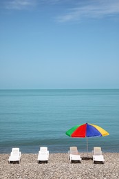 Beautiful view of umbrella and sunbeds on pebble beach near sea