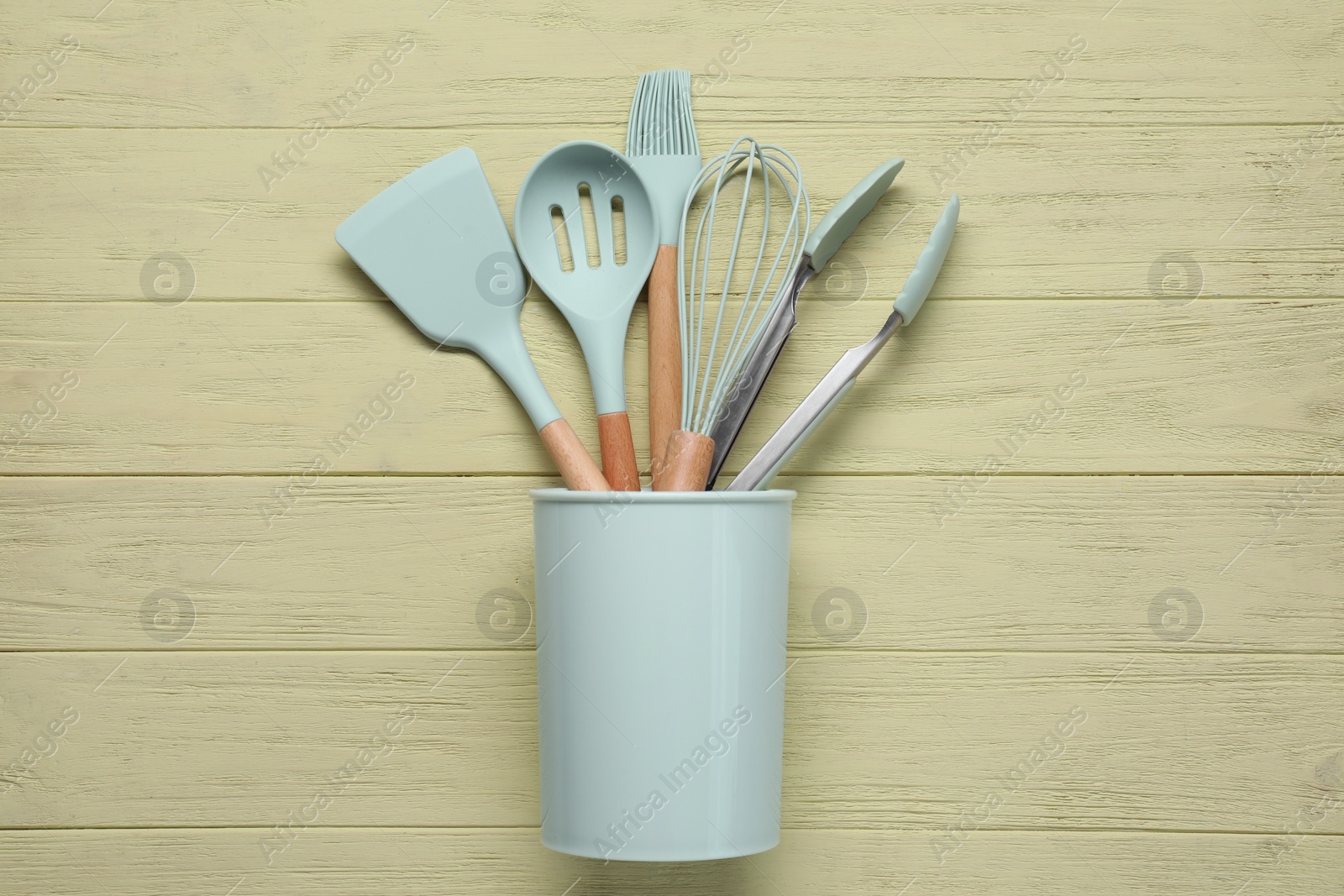 Photo of Set of kitchen utensils in holder on pale yellow wooden table, top view