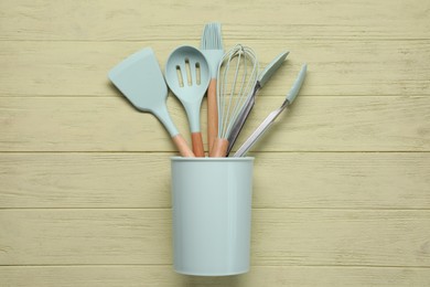 Set of kitchen utensils in holder on pale yellow wooden table, top view