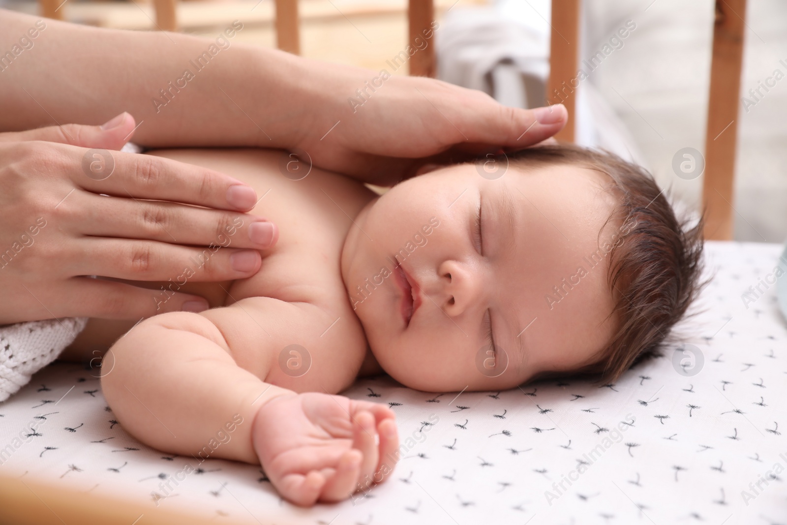 Photo of Mother covering her sleeping baby with blanket in crib at home