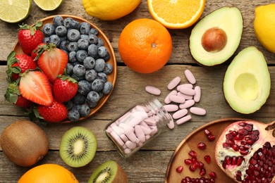 Photo of Vitamin pills in bottle and fresh fruits on wooden table, flat lay