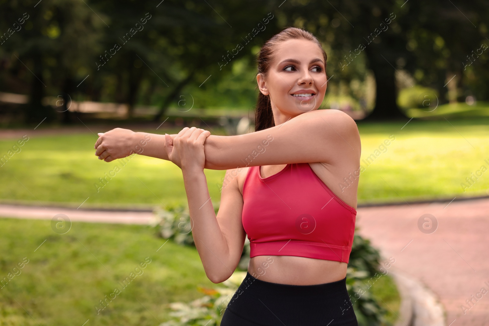 Photo of Smiling woman in sportswear stretching in park