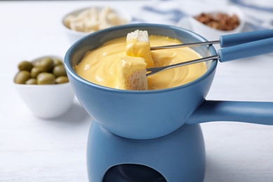 Pot of tasty cheese fondue and forks with bread on white table