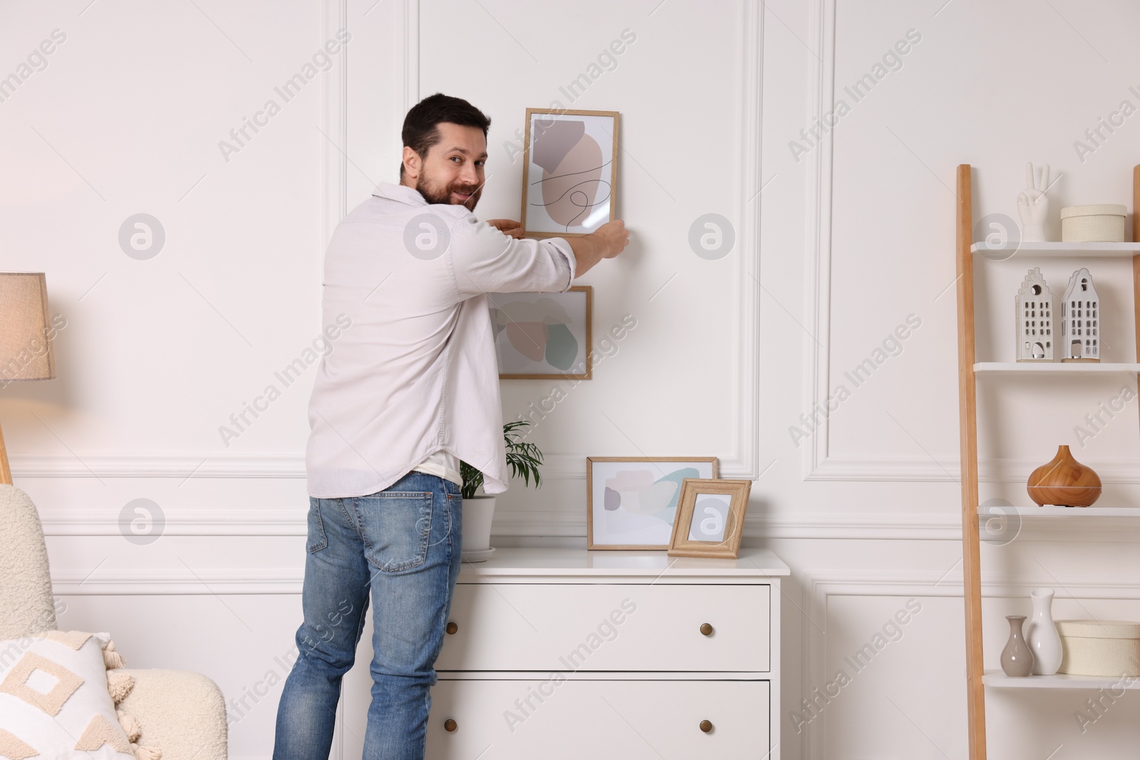 Photo of Man hanging picture frame on white wall at home