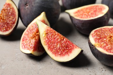 Photo of Whole and cut ripe figs on light grey textured table, closeup