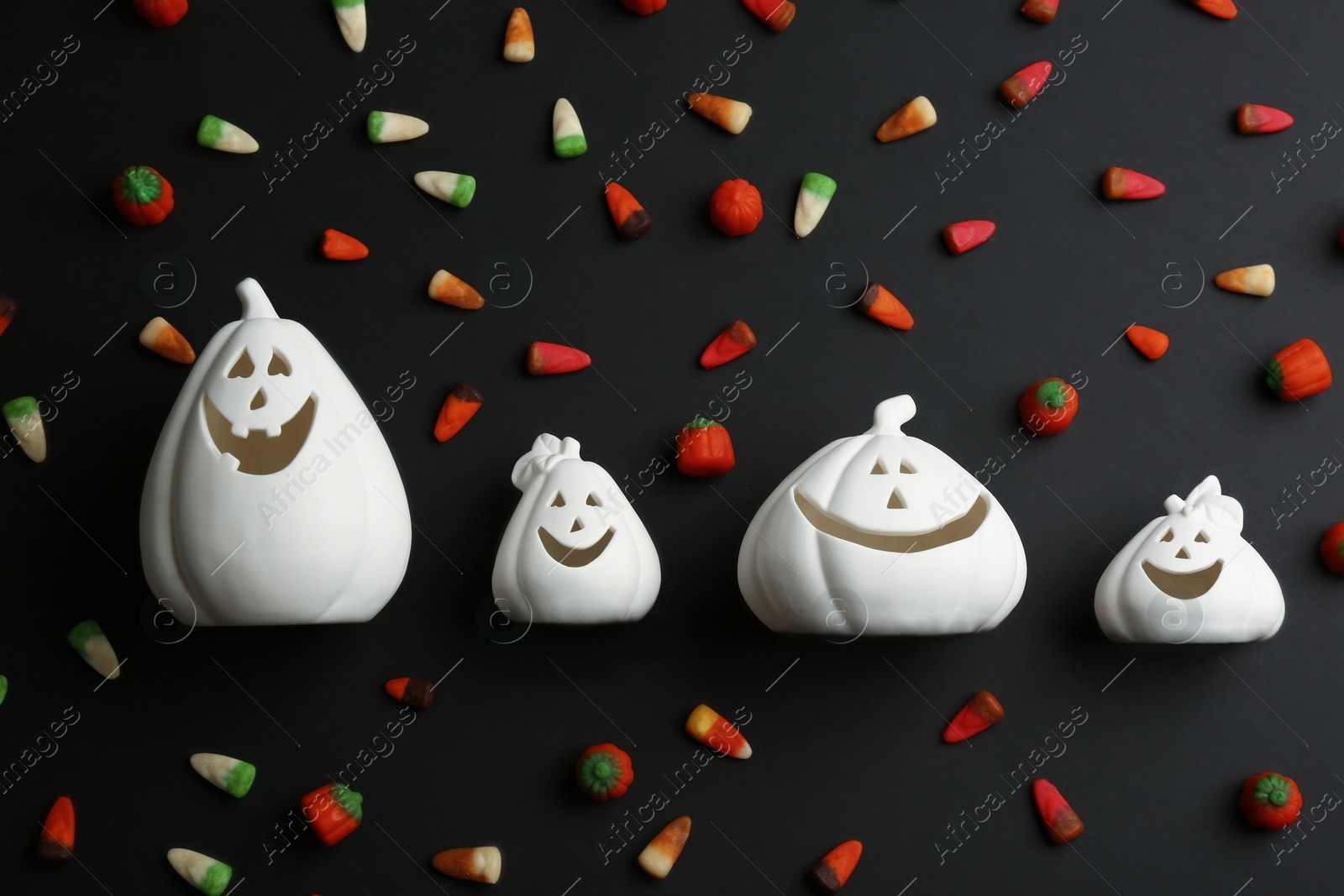 Photo of Jack-o-Lantern candle holders and jelly candies on black background, flat lay. Halloween decor