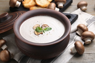 Photo of Delicious homemade mushroom soup in ceramic pot and fresh ingredients on wooden table