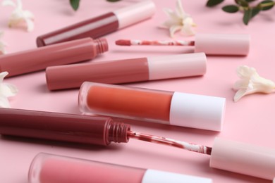 Photo of Different lip glosses, applicators and flowers on pink background, closeup