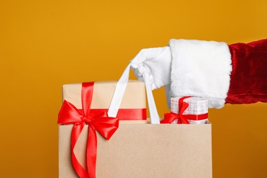 Santa holding paper bag with gift boxes on orange background, closeup