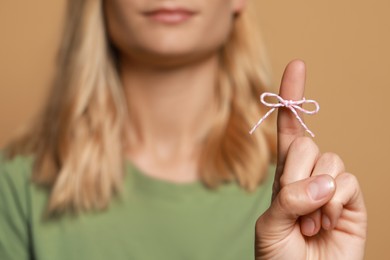 Woman showing index finger with tied bow as reminder against light brown background, focus on hand