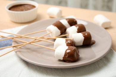 Photo of Plate with marshmallows dipped into chocolate fondue on table