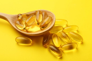 Vitamin capsules in wooden spoon on yellow background, closeup