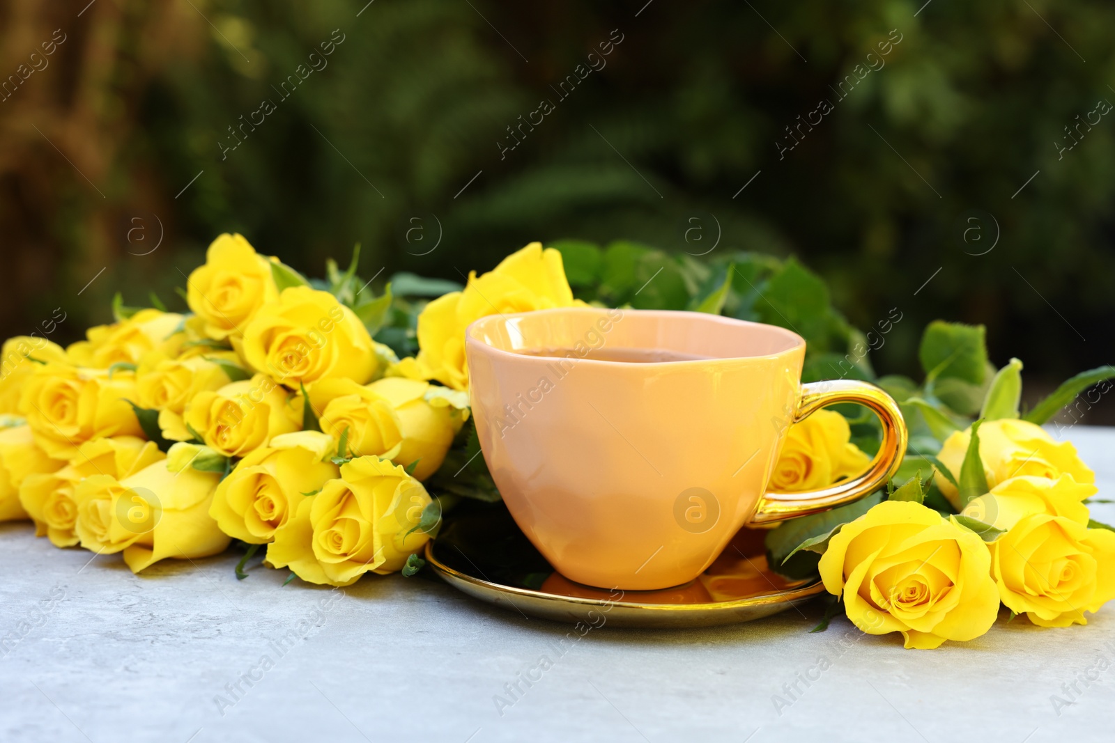 Photo of Cup of drink and beautiful yellow roses on light table outdoors