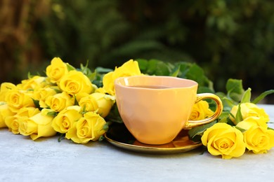 Cup of drink and beautiful yellow roses on light table outdoors