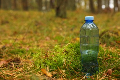 Plastic bottle of fresh water on ground in forest, space for text
