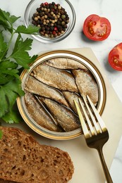 Photo of Tin can with tasty sprats and fork served on white marble table, flat lay