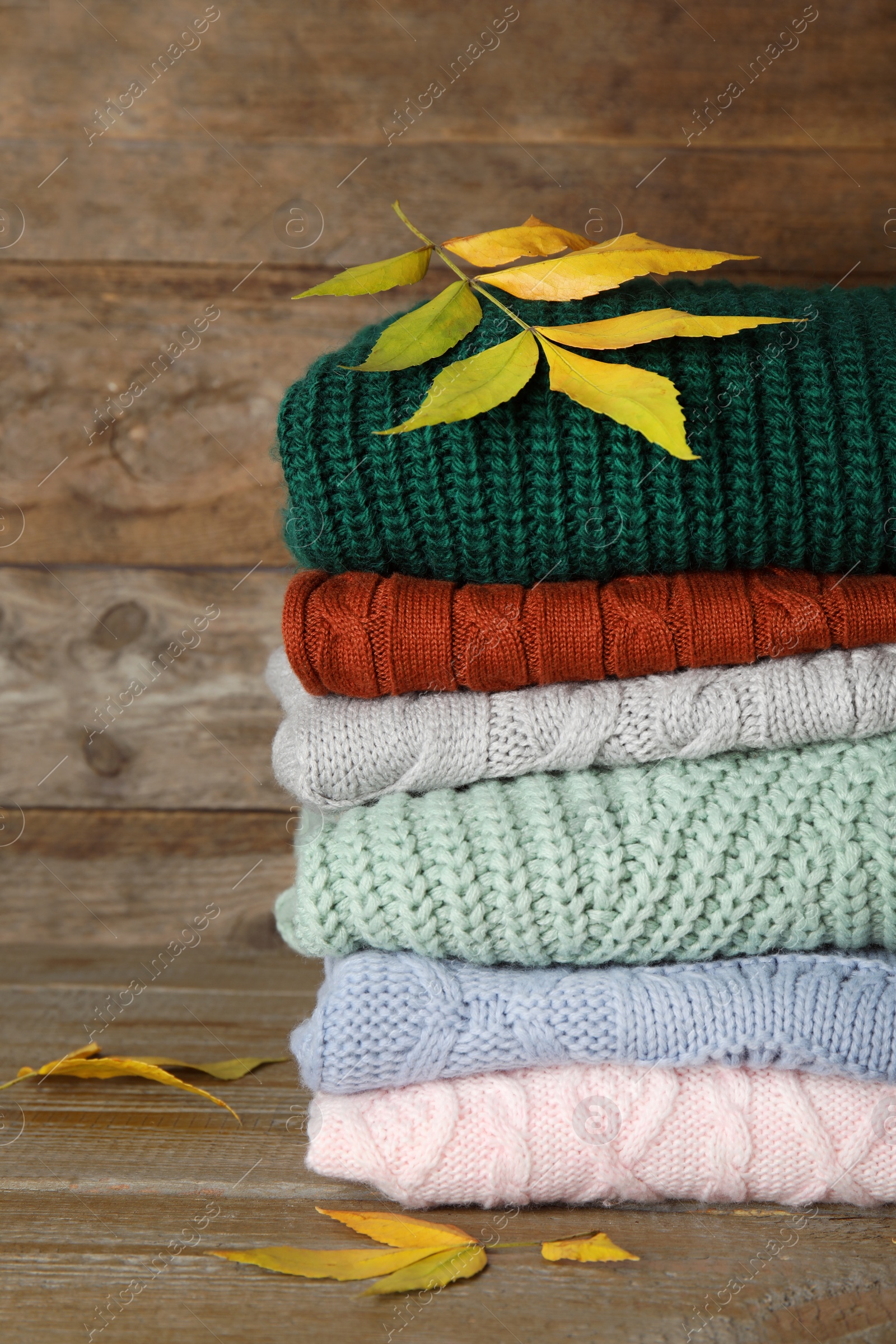 Photo of Stack of warm knitted clothes and autumn leaves on wooden background