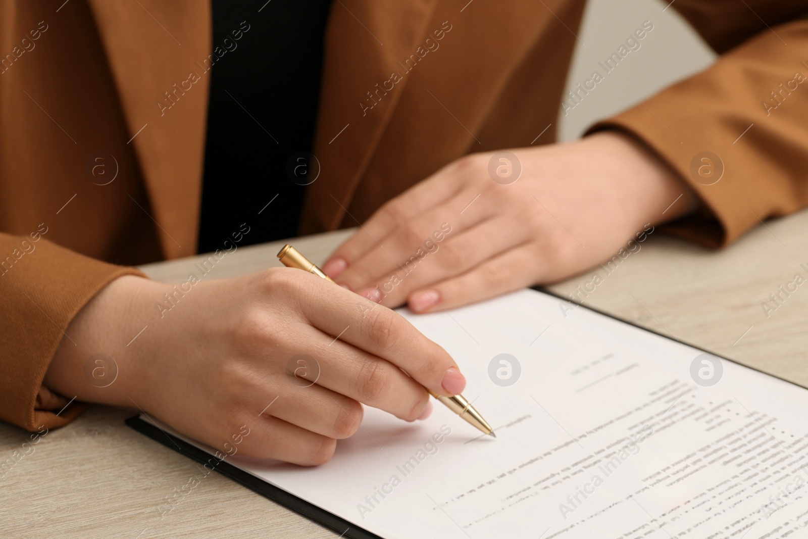 Photo of Woman signing document at wooden table, closeup