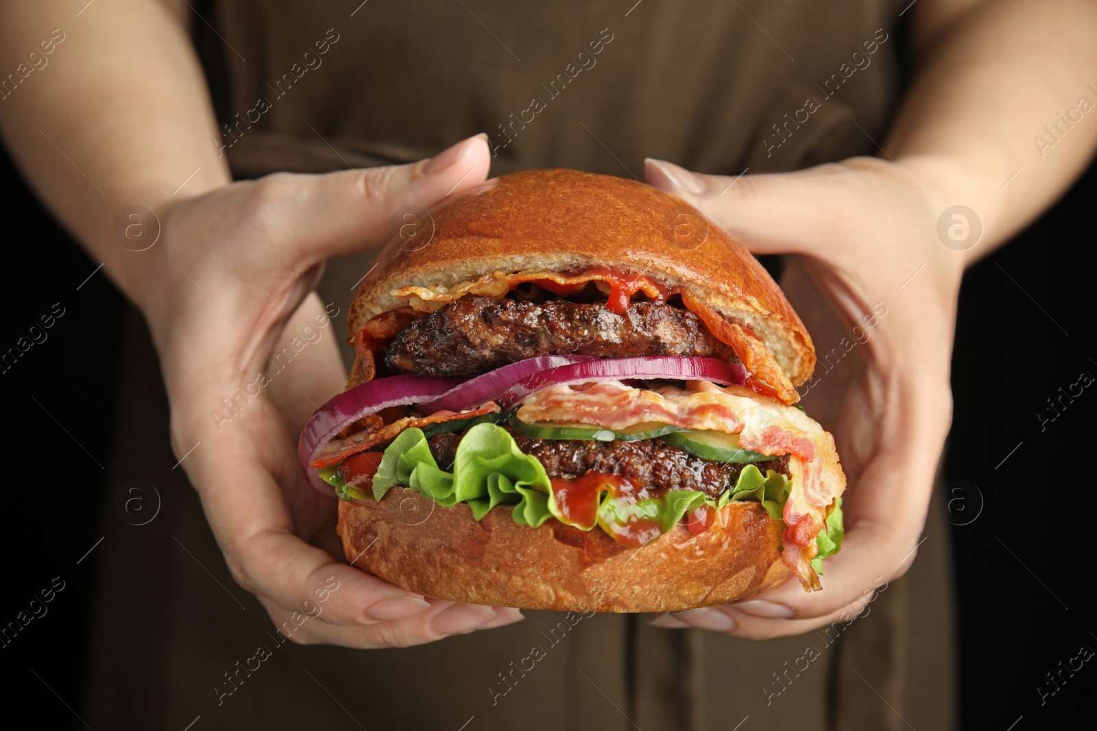 Photo of Woman holding tasty burger with bacon on black background, closeup