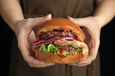Woman holding tasty burger with bacon on black background, closeup