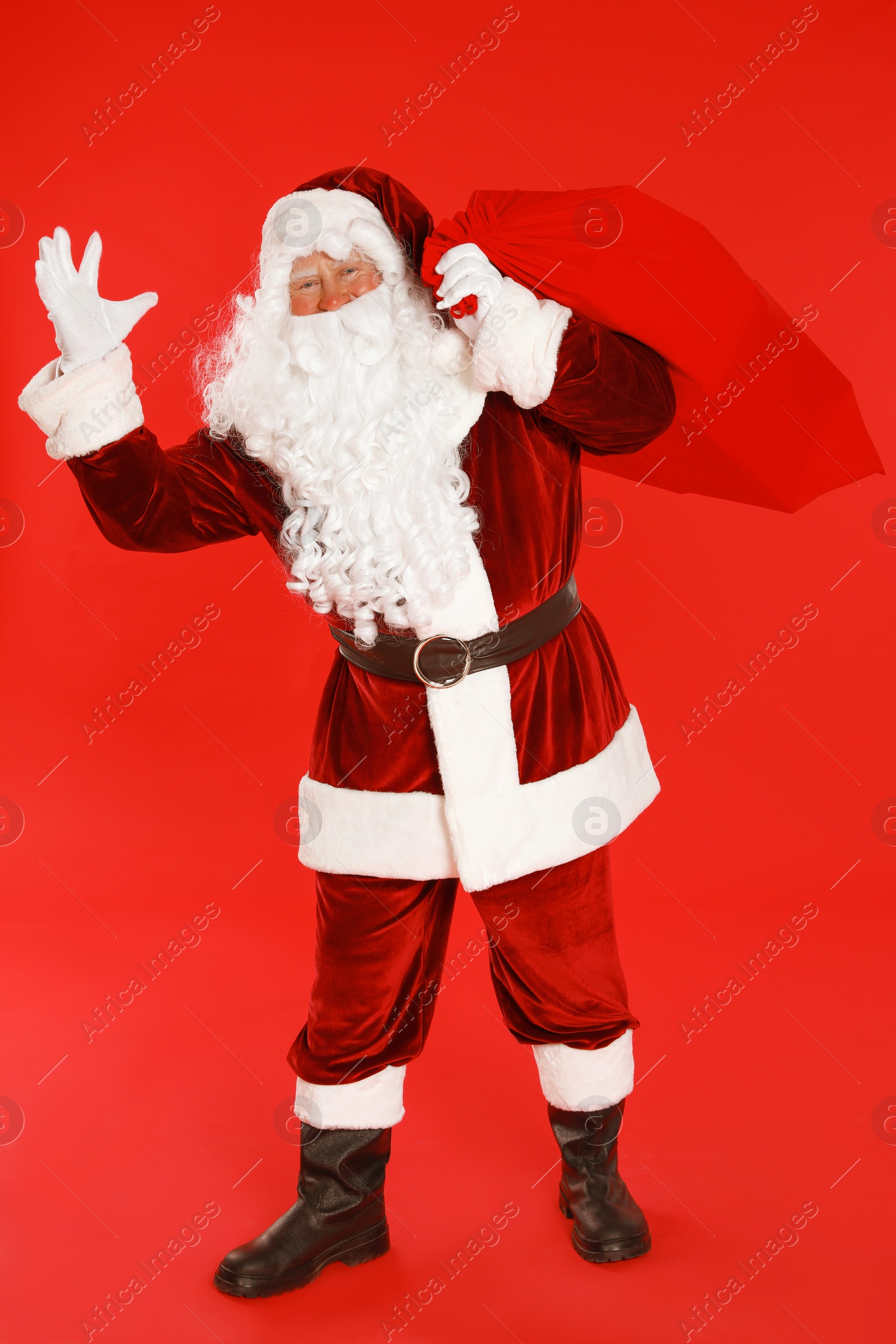 Photo of Authentic Santa Claus with bag full of gifts on red background