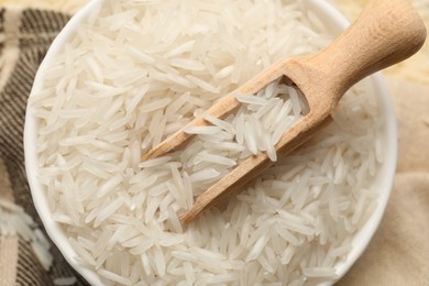 Photo of Raw basmati rice in bowl and scoop on cloth, top view