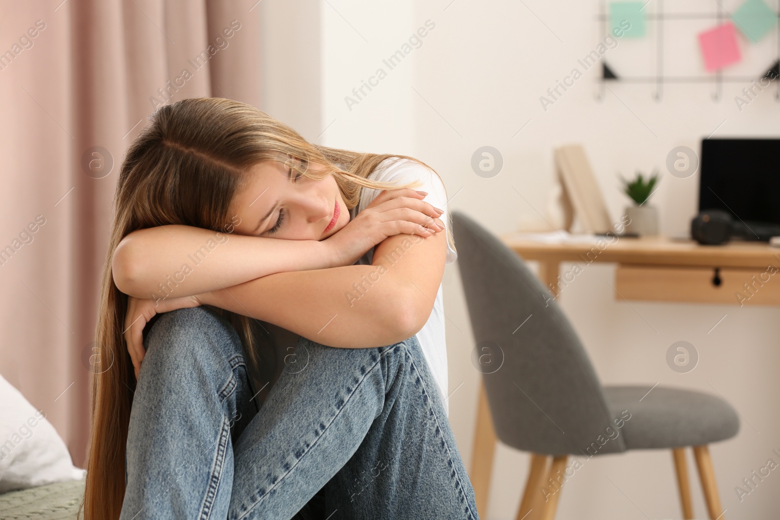 Photo of Unhappy teenage girl sitting in room at home